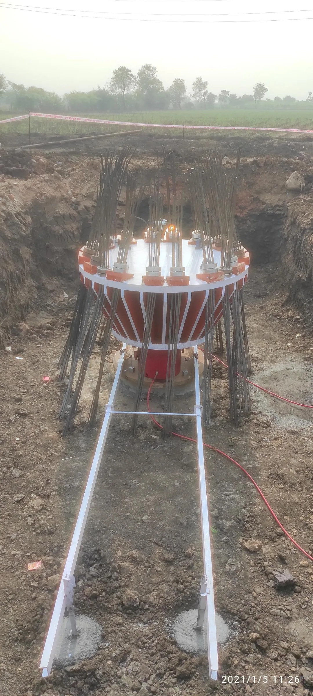 Static load test image from a construction site, indicating pile, hydraulic jack, steel crown and ground anchors.